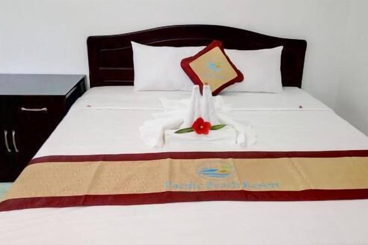 A neatly made bed with a red and beige bedspread, a white pillow, and a decorative item resembling a flower.