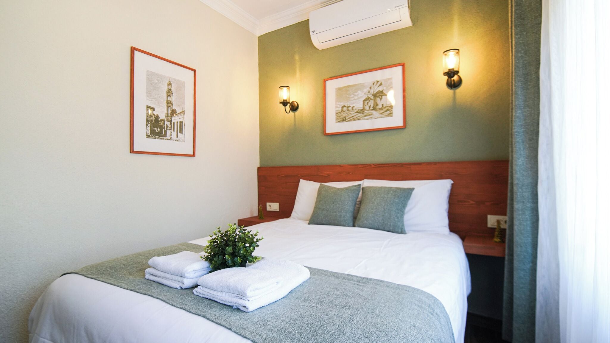 Una habitación de hotel con una cama, dos lámparas de pared y dos cuadros enmarcados.