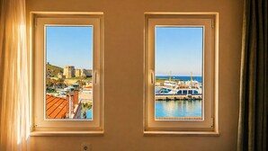 Dos ventanas con vistas a una fortaleza histórica y un puerto deportivo con barcos.