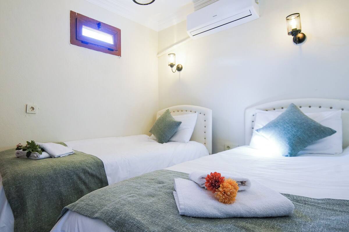 Une chambre d’hôtel avec deux lits, une petite fenêtre, un climatiseur et un luminaire fixé au mur.