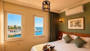 Habitación de hotel con cama, dos ventanas que dan al puerto, aire acondicionado montado en la pared y un cuadro enmarcado.