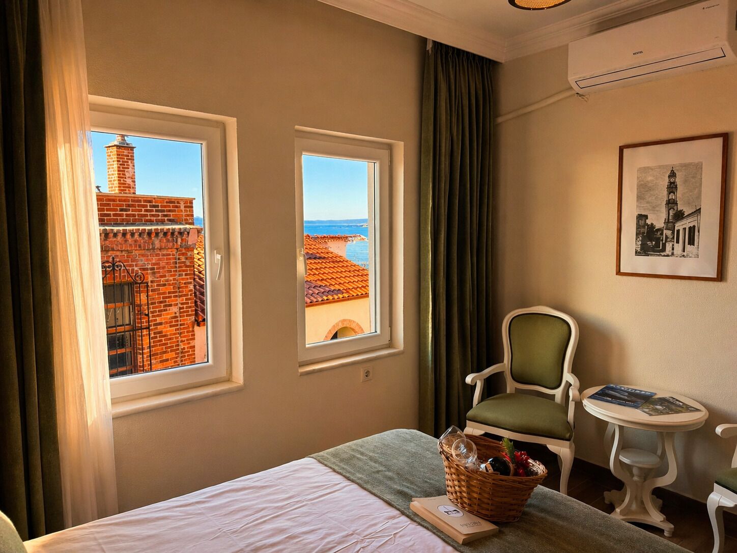 A hotel room with two windows, a bed, a chair, a small table, and a wall-mounted air conditioner.