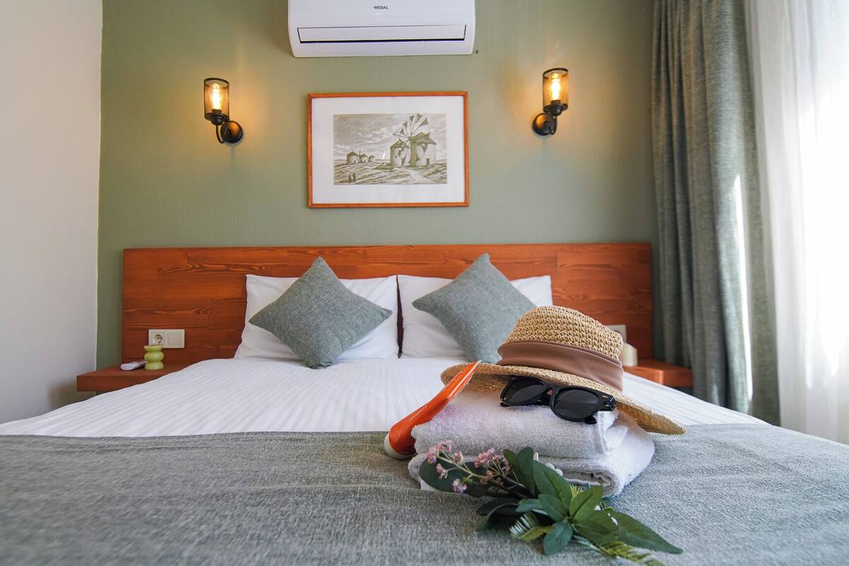 Une chambre d’hôtel avec une tête de lit en bois, deux lampes fixées au mur, un tableau encadré et un lit avec des oreillers et une serviette.