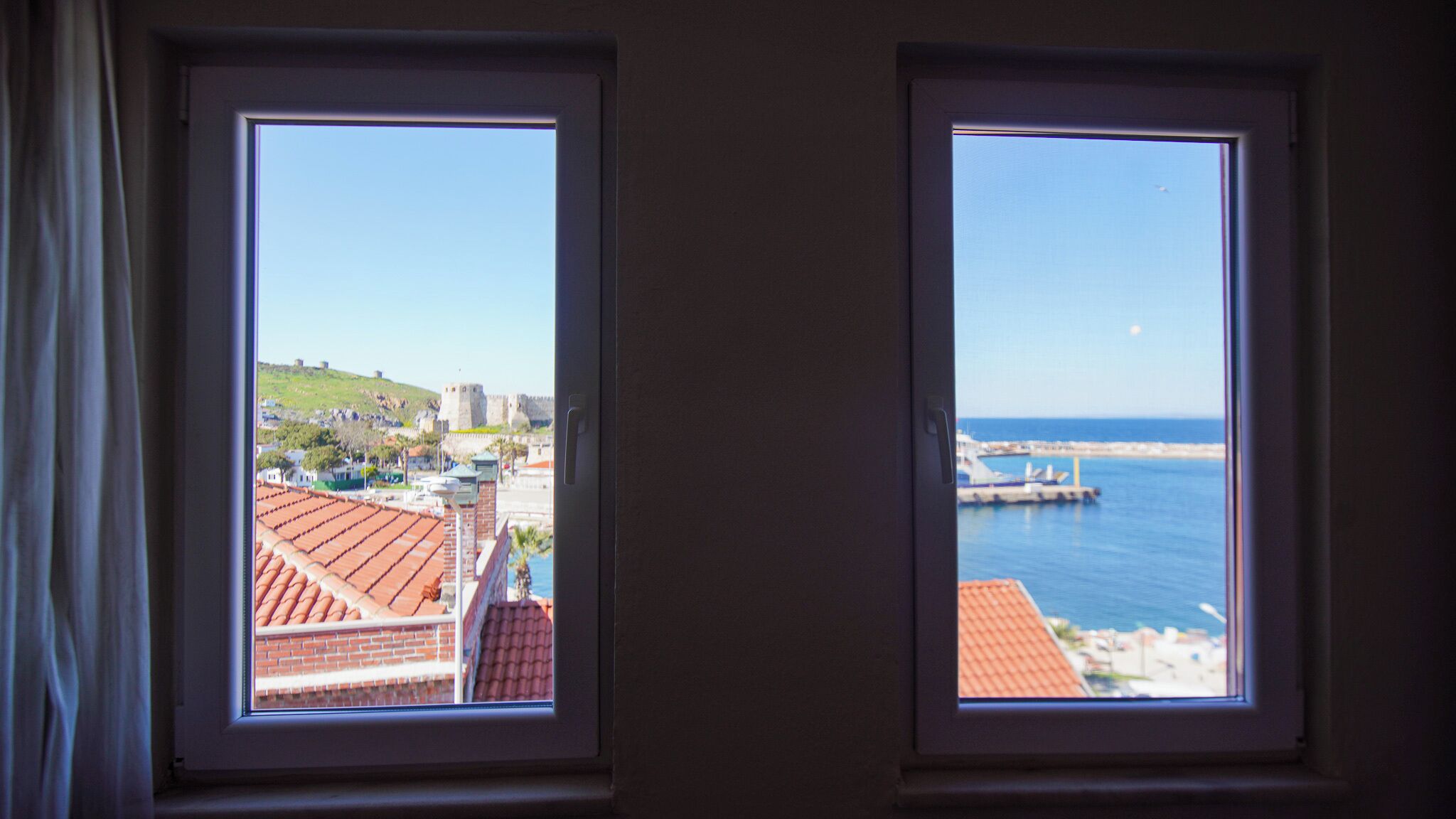 Two windows with views of a coastal town, including a castle and a pier.
