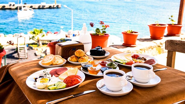 Una mesa con alimentos para el desayuno y una taza de café, con vista a un puerto deportivo lleno de barcos.