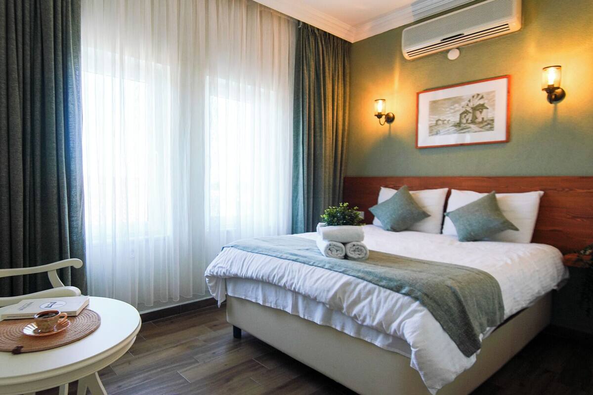 Une chambre d’hôtel avec un lit, une chaise, une table et une fenêtre avec des rideaux.