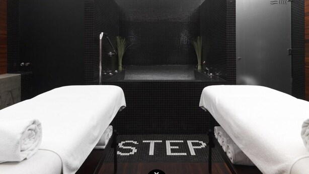 A spa room with two white towels on beds, a tiled floor with 'STEP' marked, and a mirrored wall. - HOTelarnia (Puszczykowo)