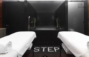 A spa room with two white towels on beds, a tiled floor with 'STEP' marked, and a mirrored wall. - HOTelarnia (Puszczykowo)