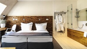 A modern hotel room with a large bed, a wooden headboard, a shower area, and a bathroom with a bathtub and a glass-enclosed shower. - HOTelarnia (Puszczykowo)