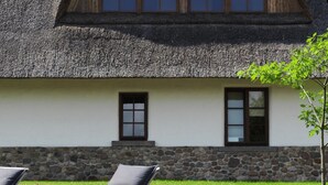 A building with a thatched roof, stone foundation, and two windows with dark frames. - HOTelarnia (Puszczykowo)