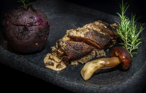 Un steak accompagné de champignons et d’une betterave, le tout servi sur une assiette en ardoise.