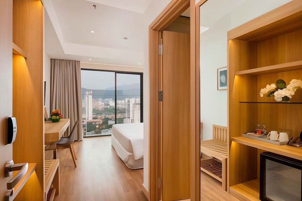 A modern hotel room with a bed, a desk, a chair, a television, and a view of the city.
