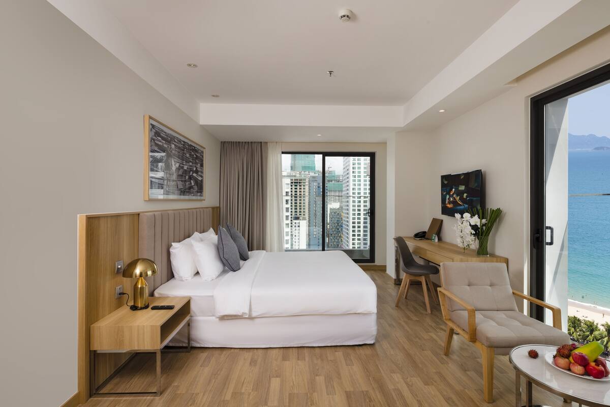 Habitación de hotel moderna con cama, escritorio, silla y vista al océano.
