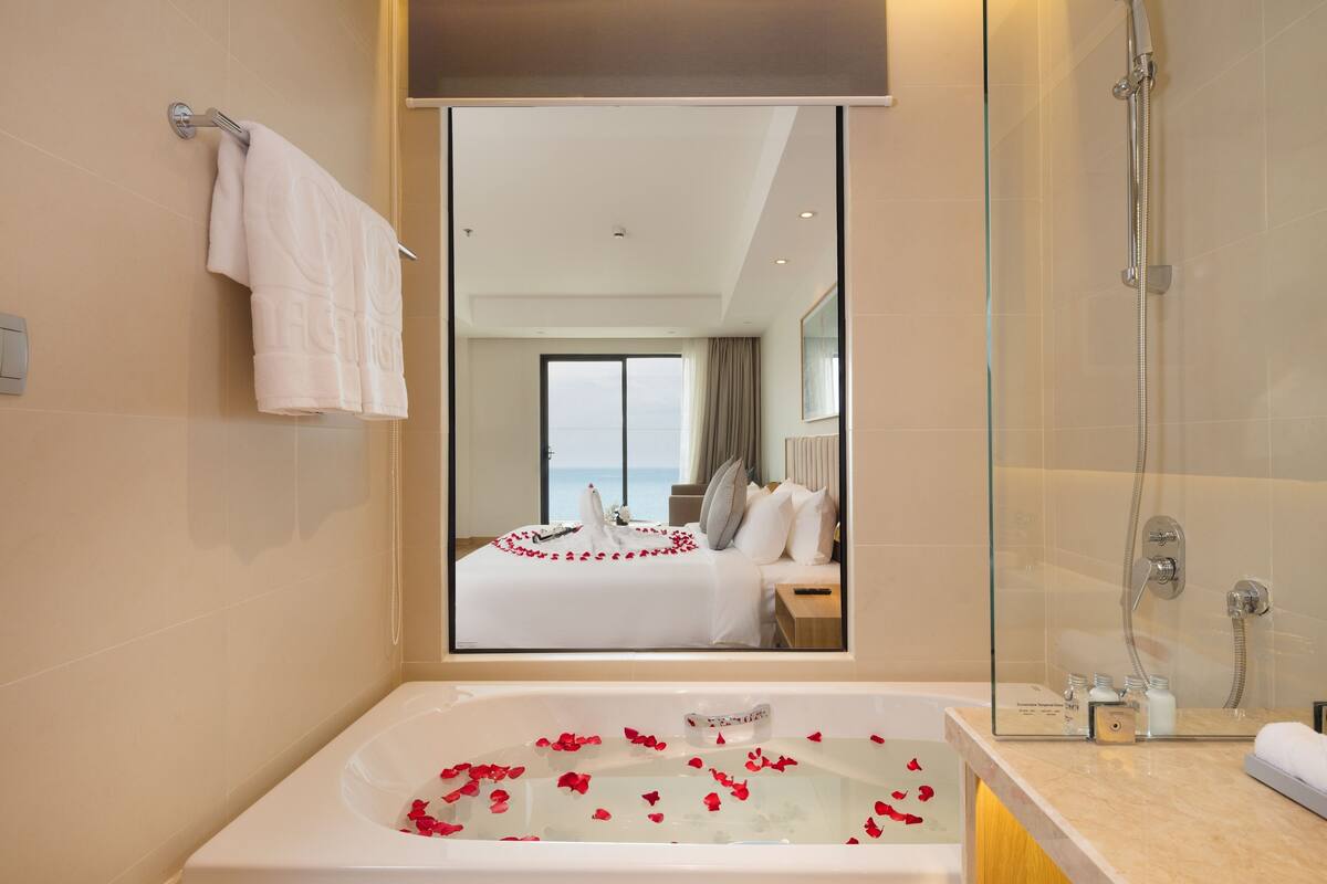 Un baño moderno con un espejo grande, una bañera con pétalos de rosa y una zona de ducha.