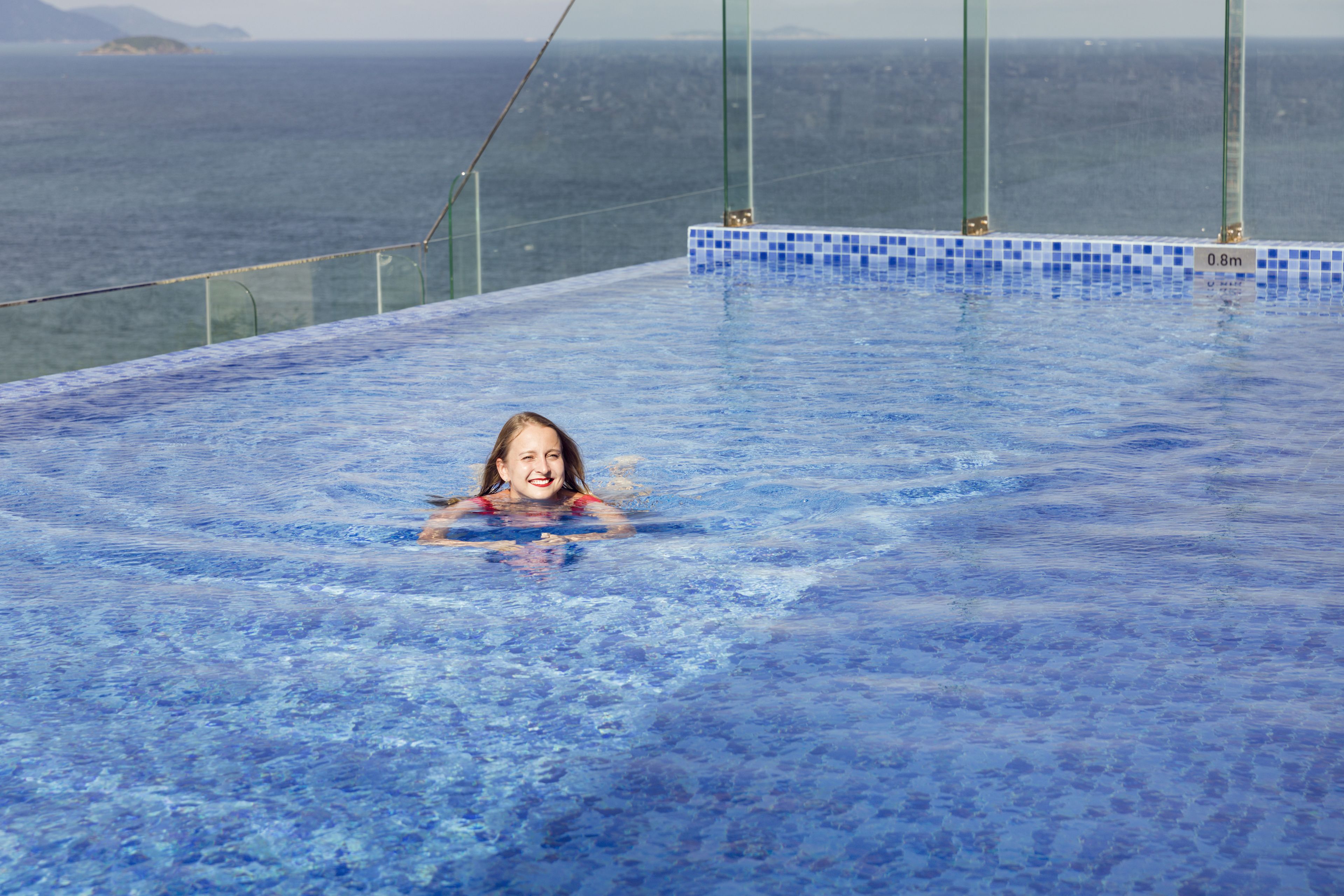 Une magnifique piscine à débordement d’un bleu profond, dotée d’une balustrade en verre, offrant une vue imprenable sur l’océan.