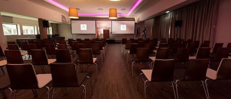 Una sala de conferencias con filas de sillas, un atril y una pantalla mostrando 'VILA GAE COLLECIO BRAGA'.