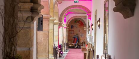 A corridor with a red carpet, stone arches, and a mural on the wall.