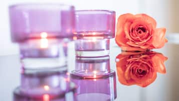 Three purple candle holders and a single orange rose on a reflective surface.