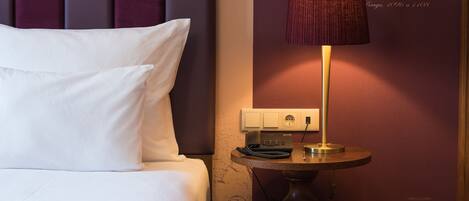 Ein Hotelzimmer mit einem großen Bett, einem Nachttisch mit Lampe und einem an der Wand hängenden Kunstwerk.