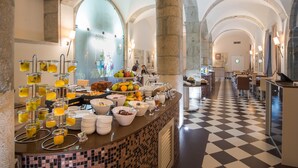 Un buffet de petit-déjeuner proposant une variété de fruits, de jus et de céréales, le tout servi dans une salle aux arches en pierre et au sol carrelé.