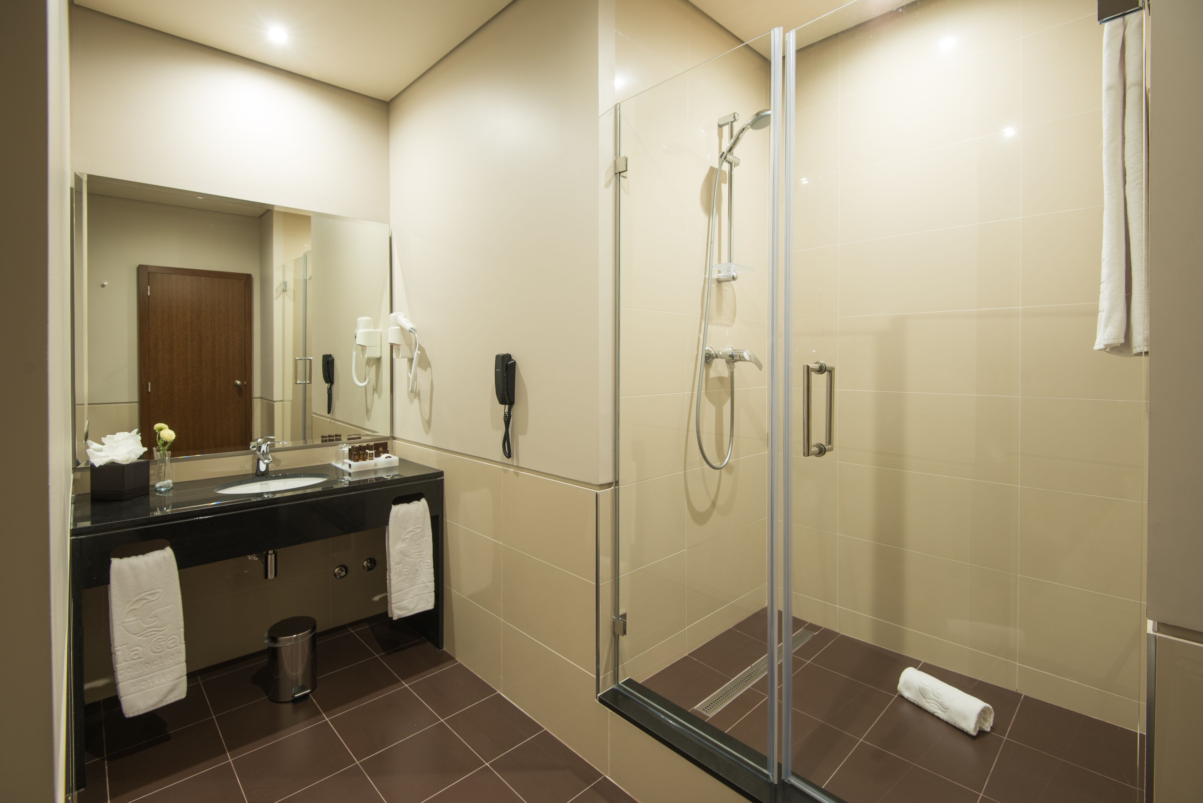 Un baño moderno con ducha de vidrio, lavamanos con espejo y dos toallas sobre el mostrador.
