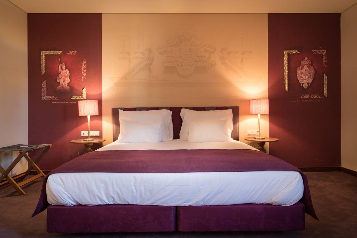 A hotel room with a large bed, two bedside lamps, and decorative wall art.