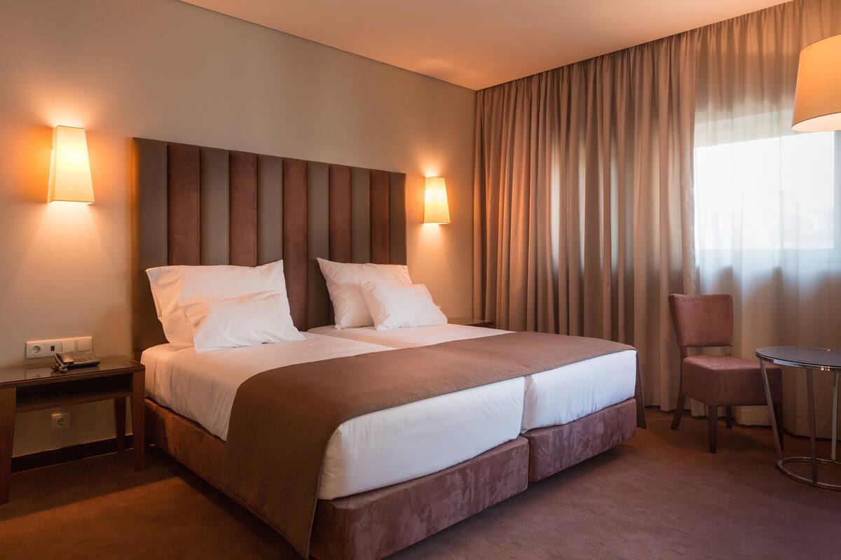 A hotel room with a large bed, two bedside lamps, a chair, and a small table.