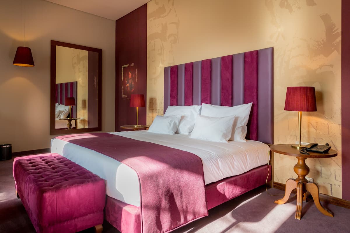 A hotel room with a large bed, a bedside table, a mirror, and a decorative wall.