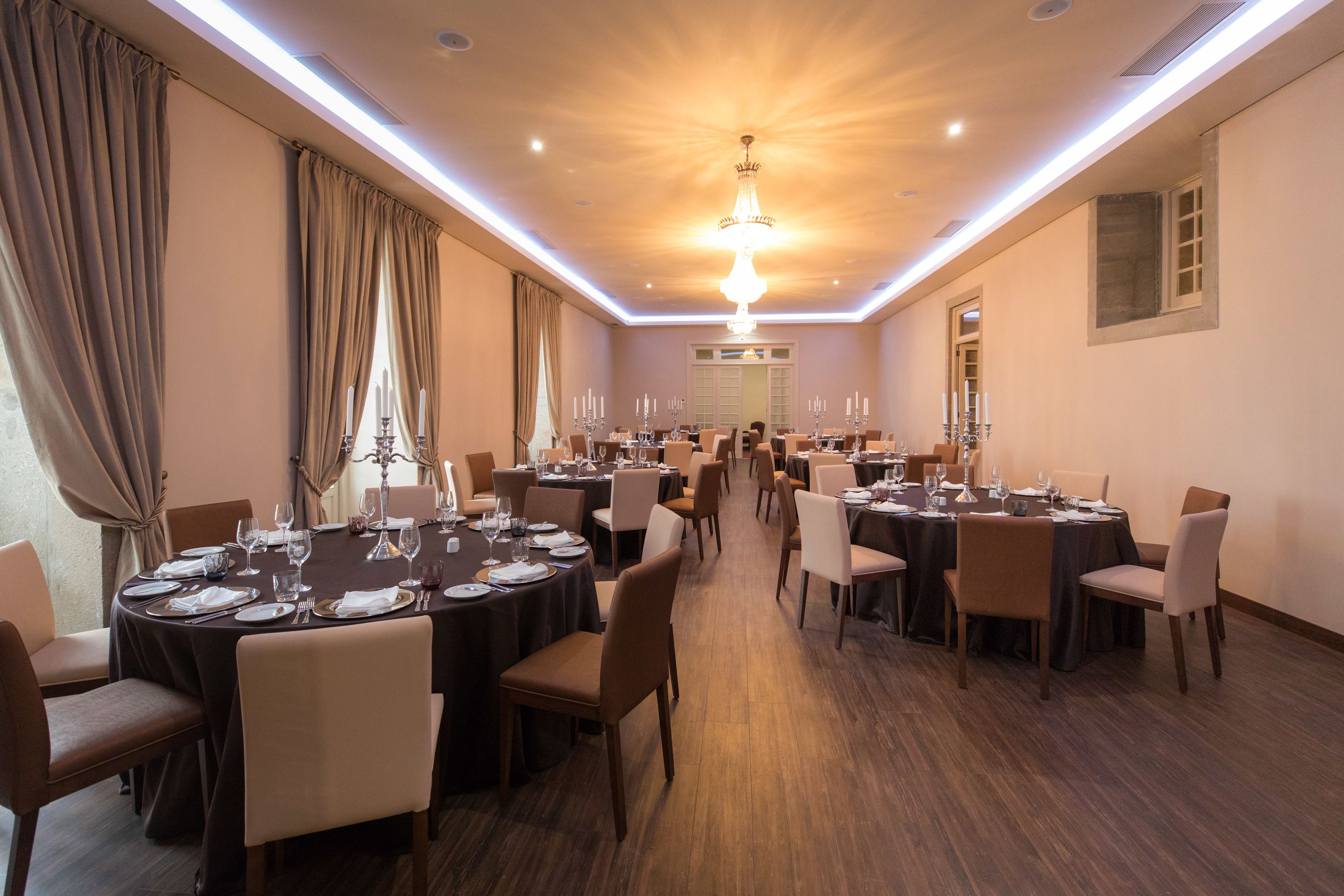 Une salle de banquet spacieuse, dotée de nombreuses tables rondes dressées pour le repas, agrémentée de centres de table à bougies et d’une décoration de table élégante.
