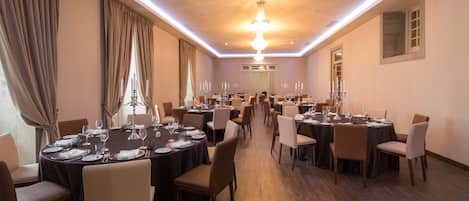 A spacious banquet hall with multiple round tables set for dining, featuring candle centerpieces and formal table settings.