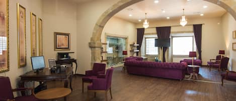 Un hall d’entrée spacieux avec un haut plafond en arc, un plancher en bois, des meubles recouverts d’un tissu violet et un écran de télévision.