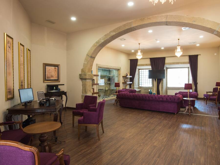 A spacious lobby with a high arched ceiling, wooden flooring, purple upholstered furniture, and a television screen.