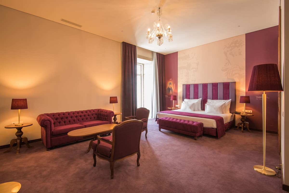 A hotel room with a bed, a sofa, a chair, a table, and a lamp.