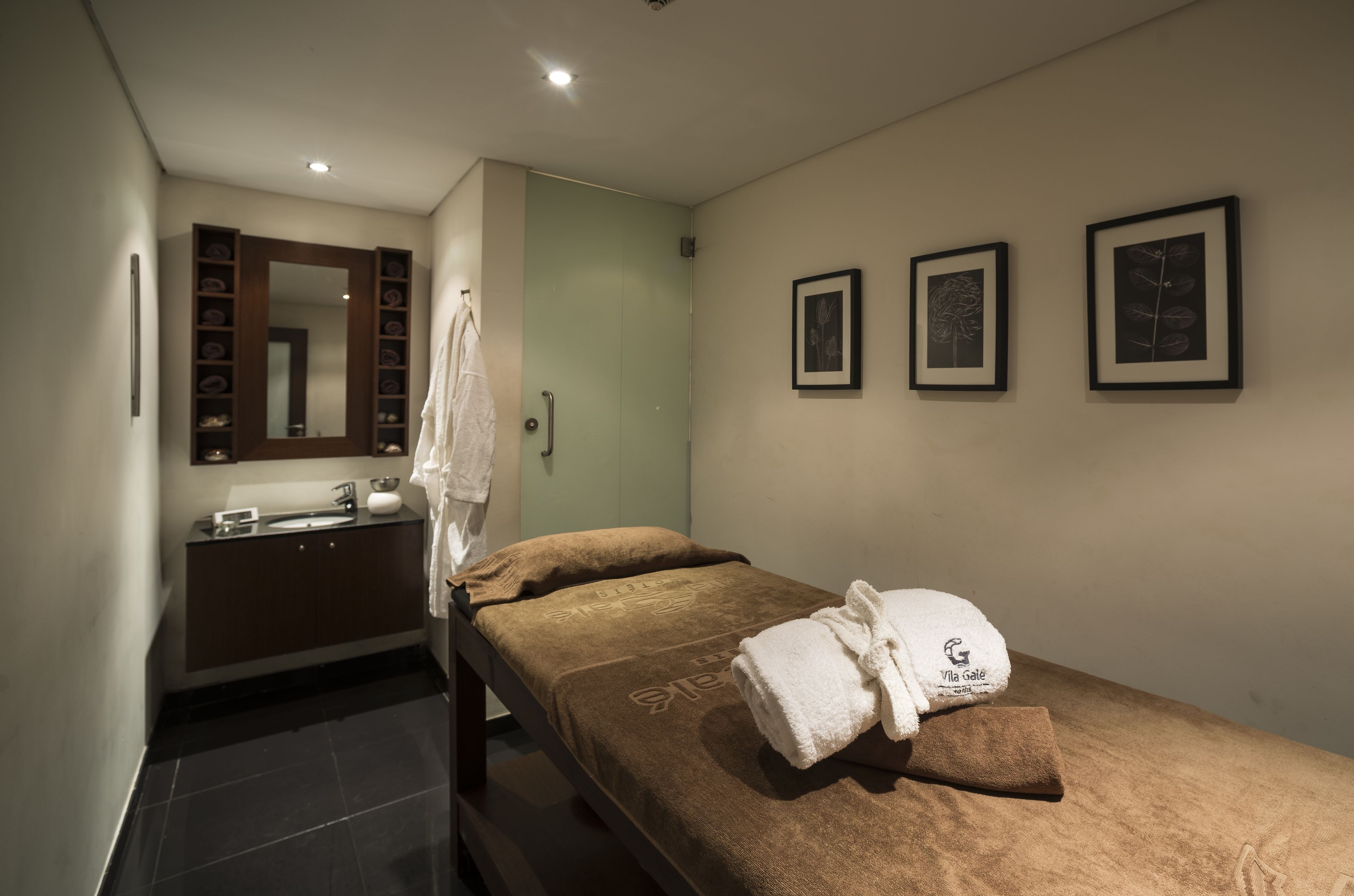 Une chambre d’hôtel avec un lit, une salle de bain comprenant un lavabo et un miroir, et des œuvres d’art encadrées accrochées au mur.