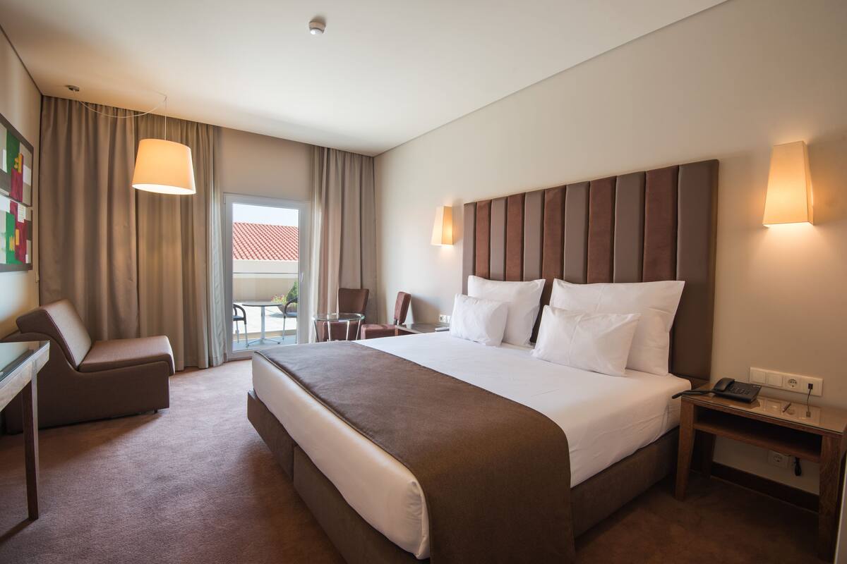 A hotel room with a large bed, a desk, a chair, and a small table.