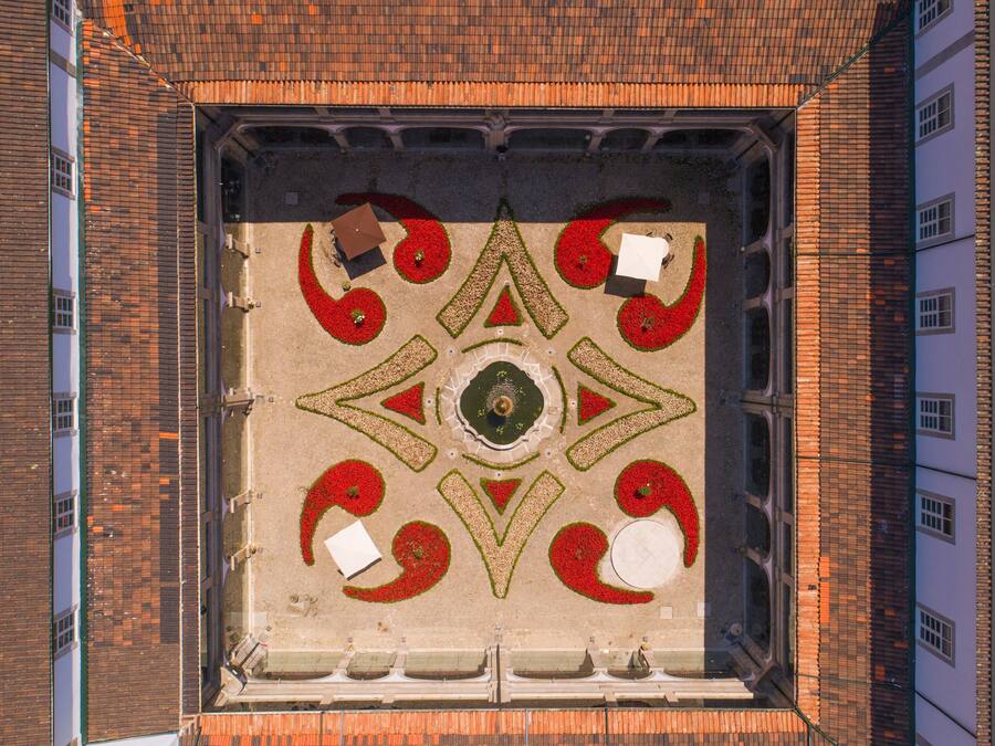 An aerial view of a courtyard with a geometric garden design, surrounded by buildings.