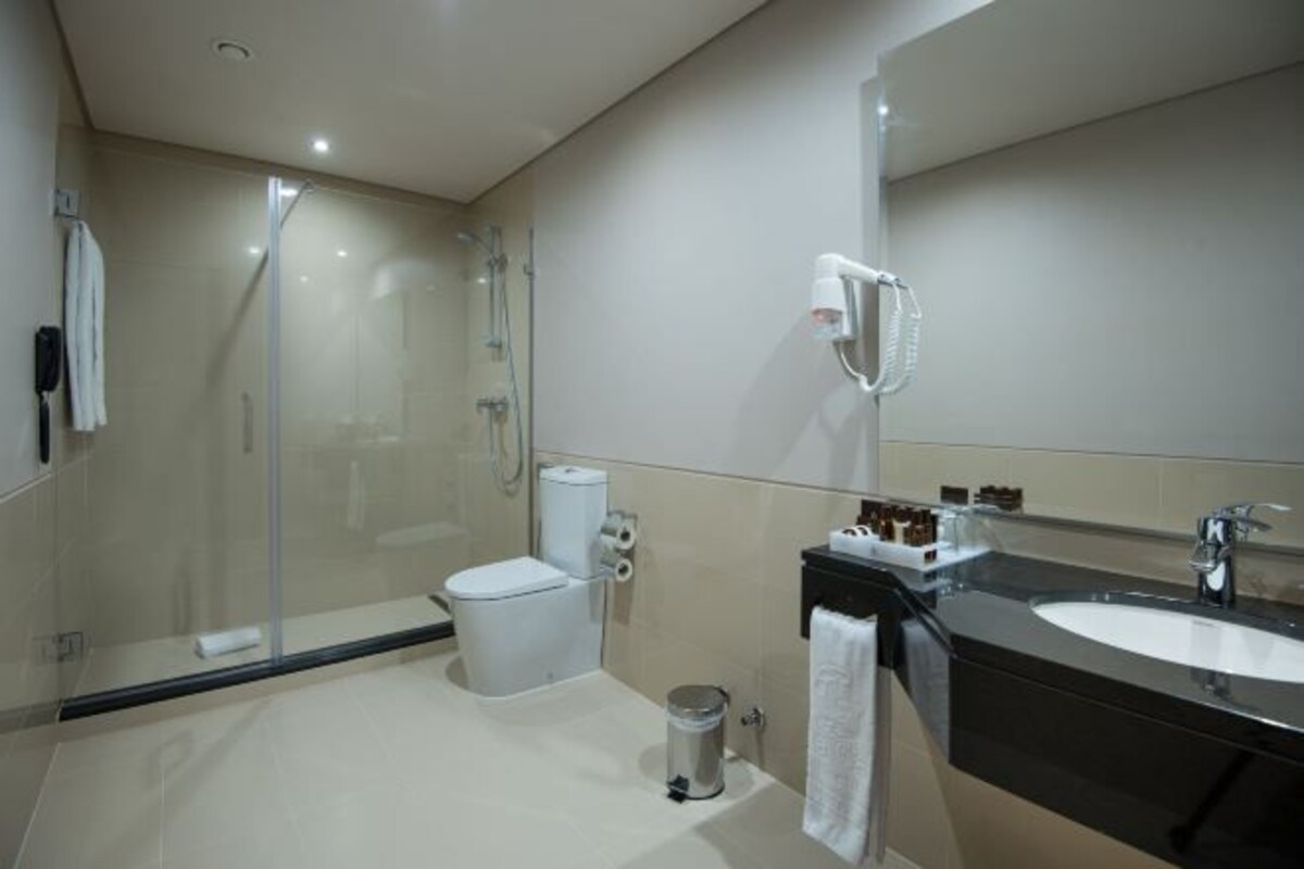 Un baño moderno con ducha envuelta en vidrio, inodoro blanco, lavamanos negro con espejo y una toalla blanca colgada en la pared.
