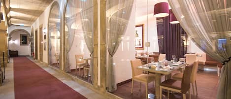 A hotel corridor with arched glass doors, a red carpet, and a dining area with tables and chairs.