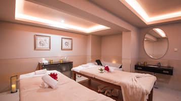 Relax in a serene spa room with two massage tables, a large mirror, and a wall-mounted shelf.