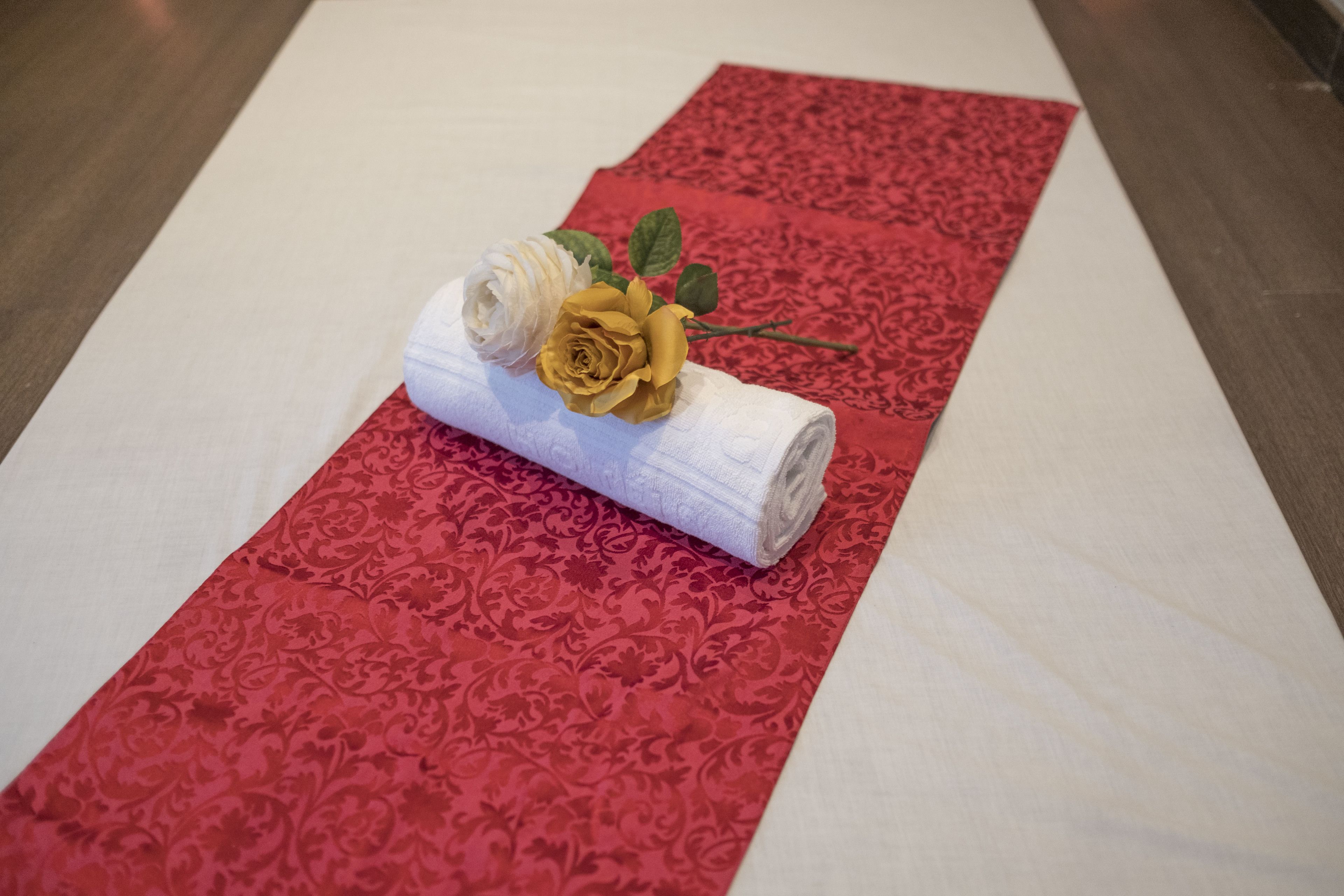 Ein roher Teppich mit einem gemusterten Muster, ein aufgerolltes weißes Handtuch und eine gelbe Rose darauf.