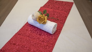 Alfombra roja con un patrón, una toalla blanca enrollada y una rosa amarilla encima.
