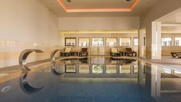 Een modern binnenzwembad met helder water, ligbedden en een plafond met oranje verlichting.
