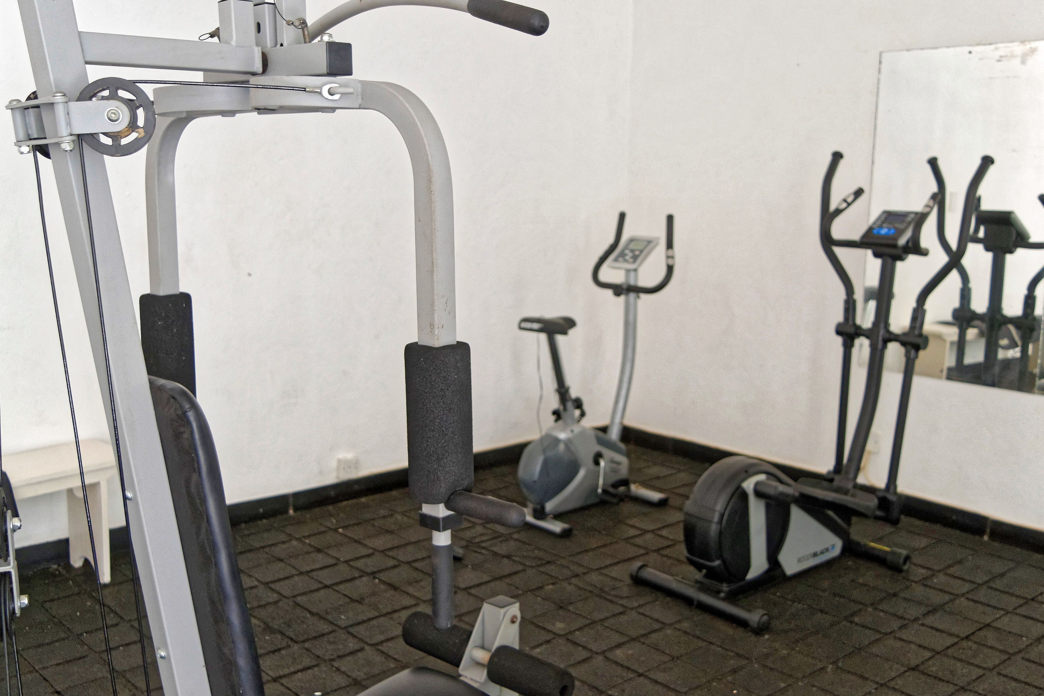 A gym with exercise equipment including a treadmill, elliptical, and weight machine.