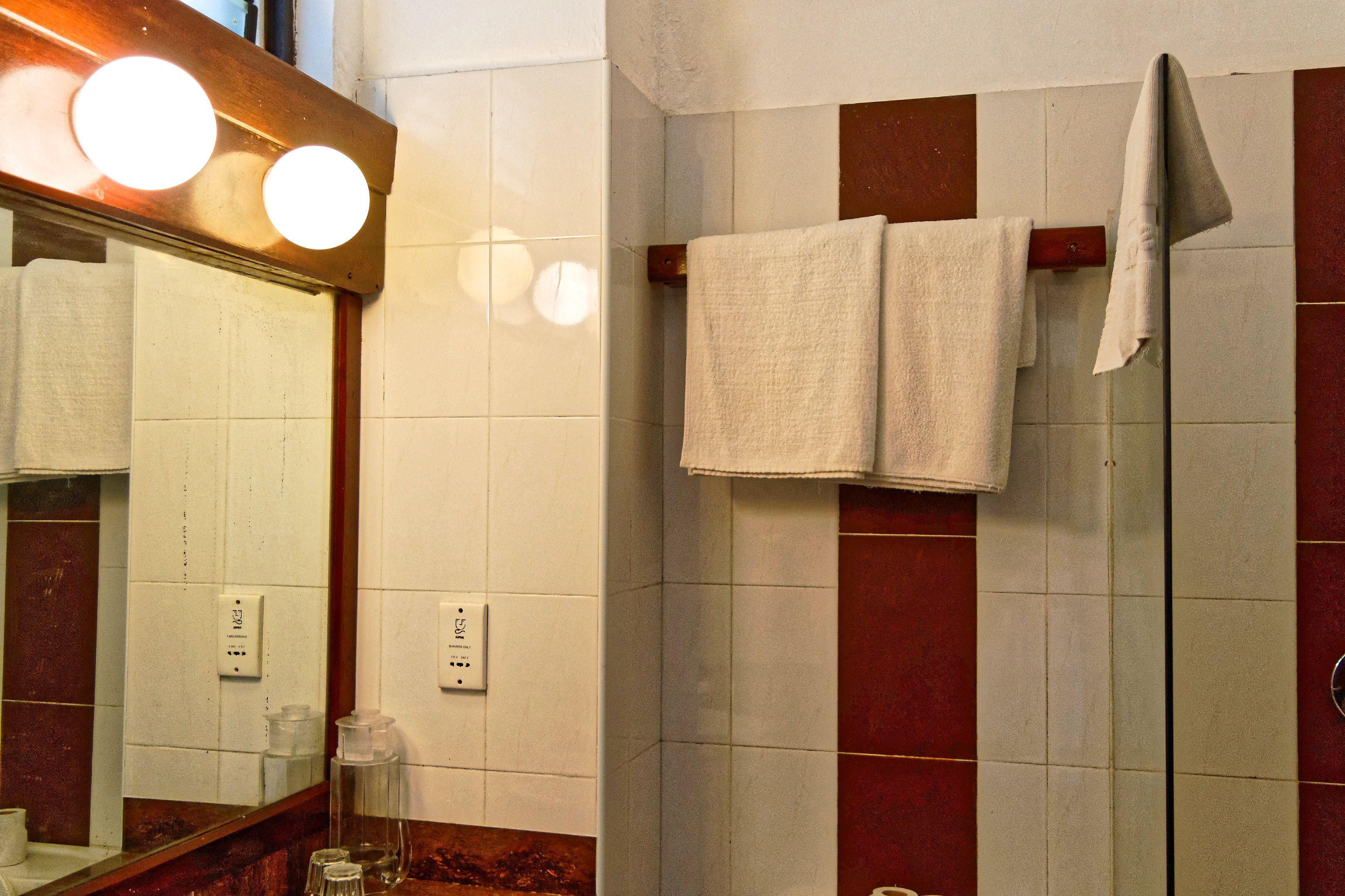 Un baño con un espejo, dos toallas colgadas en un perchero y una pared de azulejos con un diseño rojo y blanco.