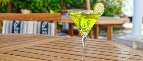 A martini glass with a lime wedge on a wooden table outdoors.