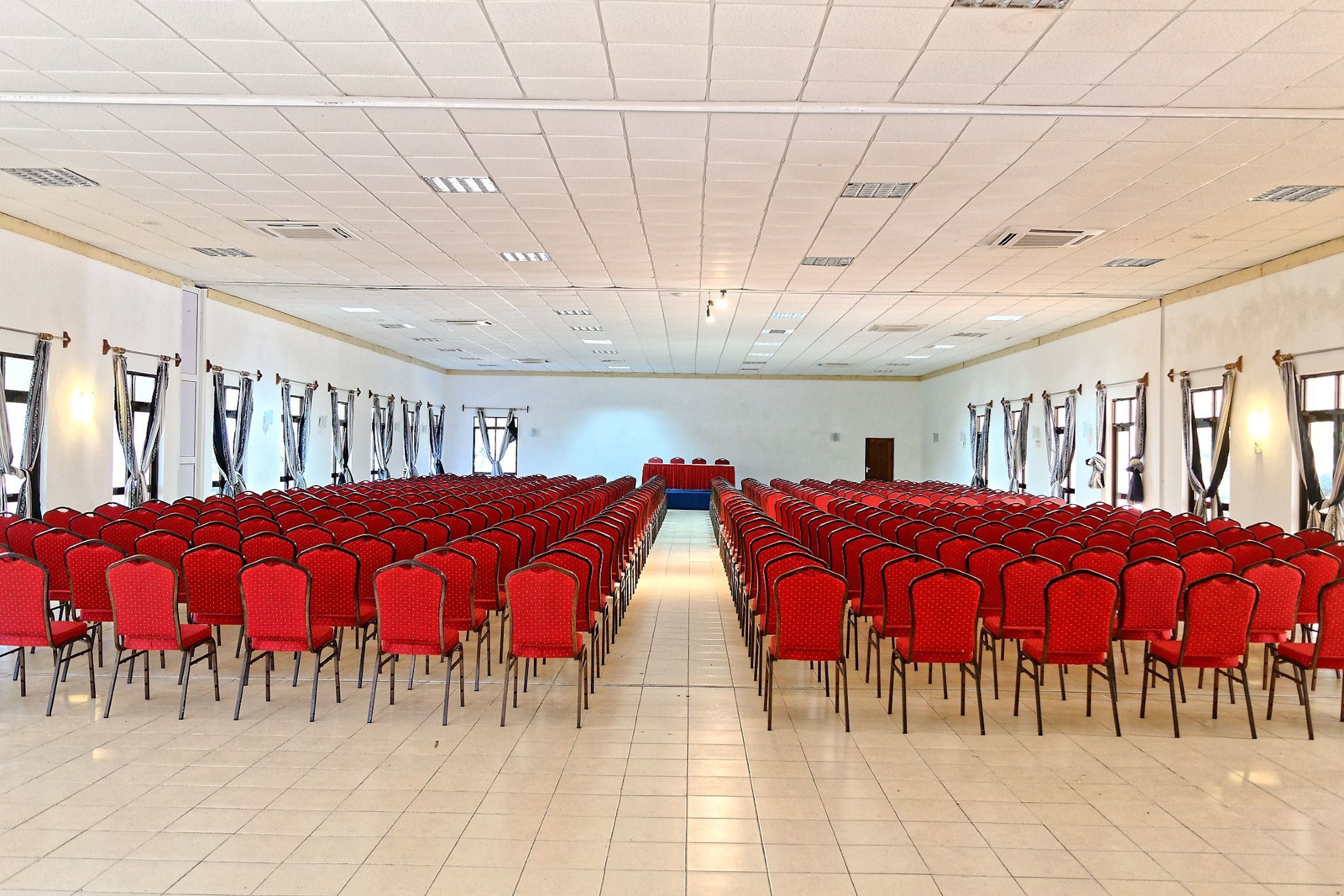 A large conference room with rows of red chairs, a stage at the front, and large windows with curtains.