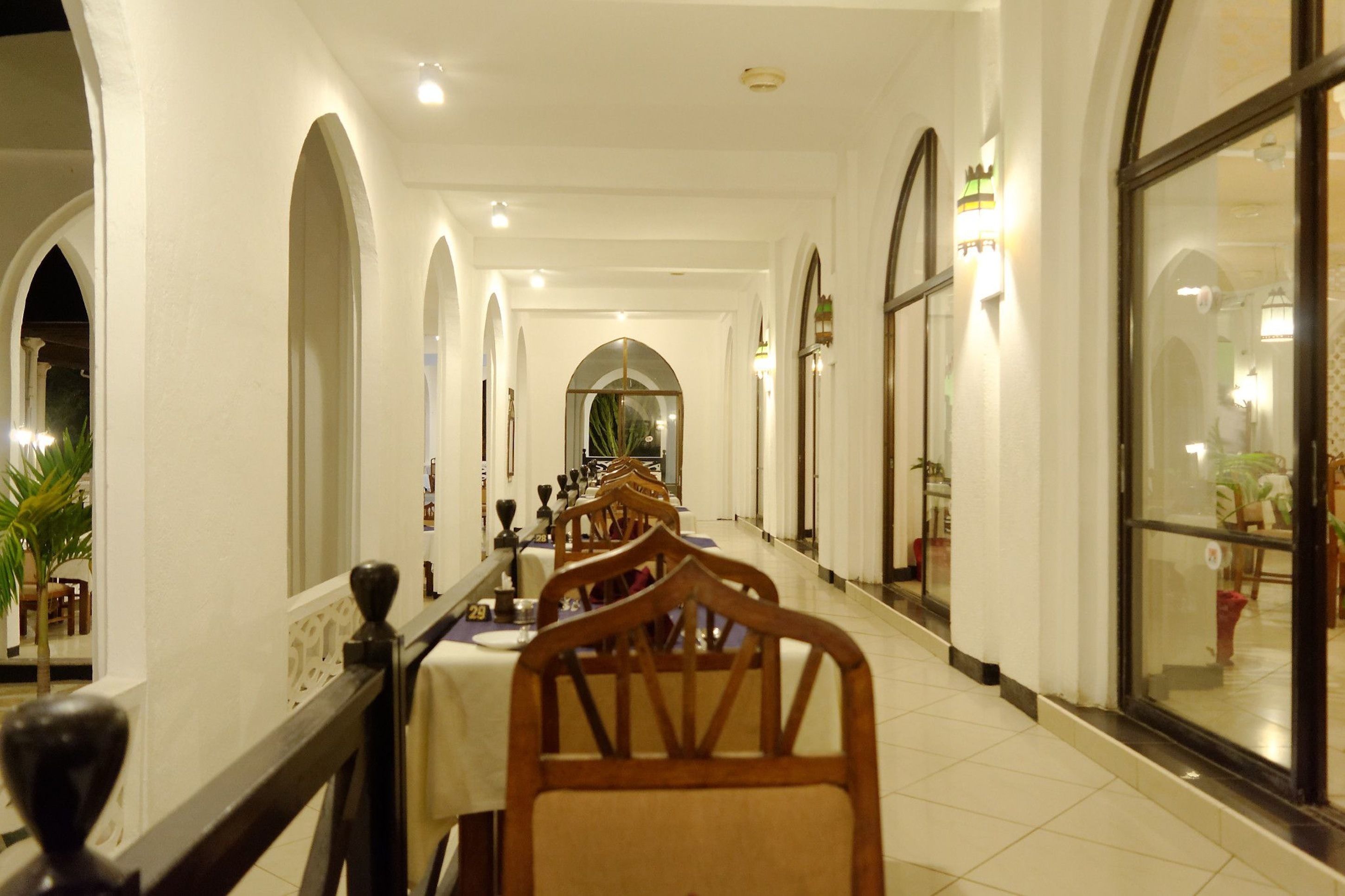 A long corridor with tables and chairs, arched doorways, and large windows.
