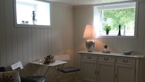 A compact living space with a dining area, a small table with a candle, a sofa with decorative pillows, a cabinet with drawers, and a window with a view of greenery. - Otra Inn (Vennesla)