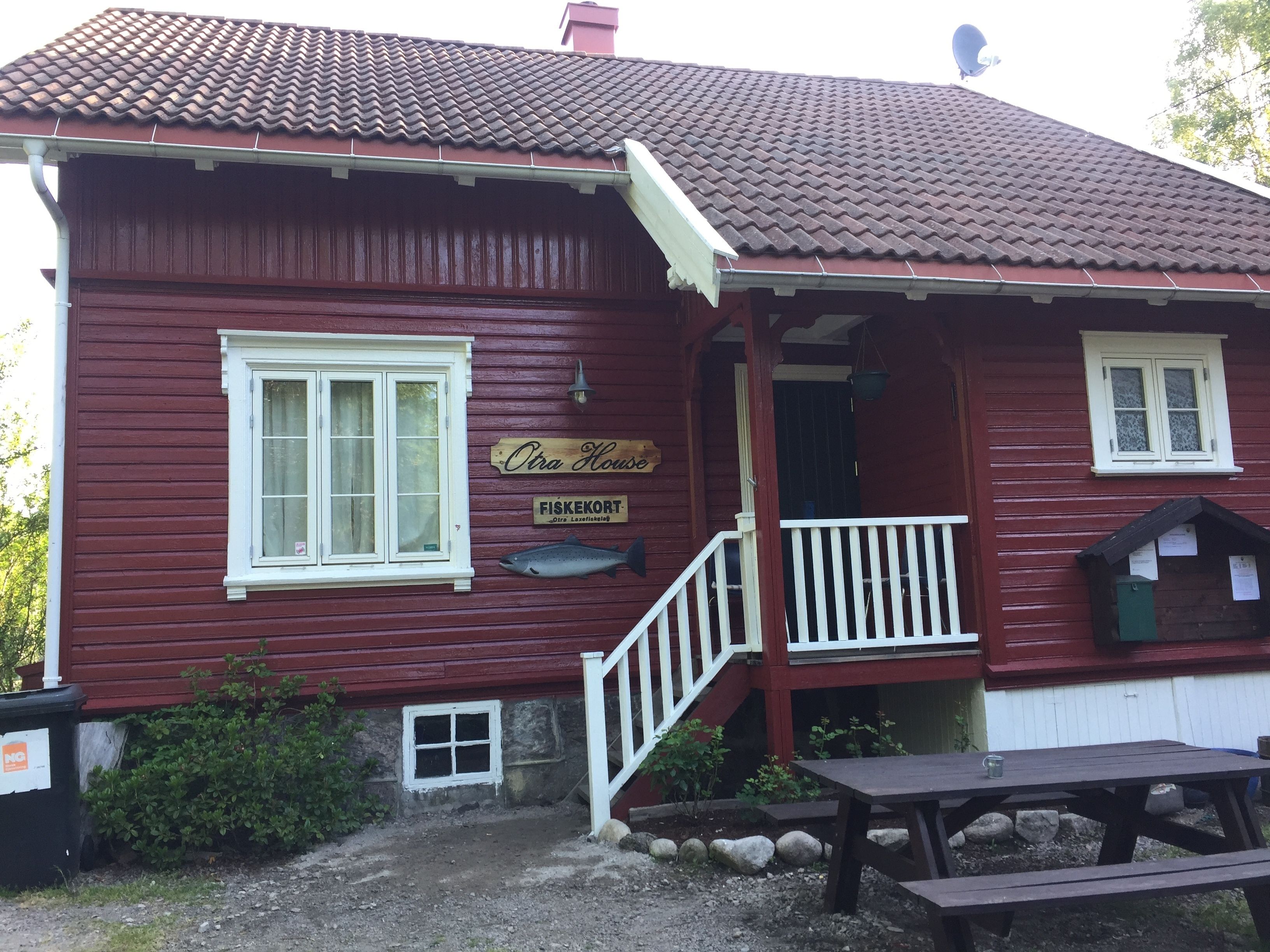 A red wooden building with a white window, a wooden sign reading "FISKEKORT," and a small outdoor seating area.