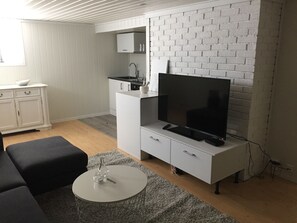 A modern living room with a flat-screen TV, a white cabinet, a grey rug, and a black sofa.